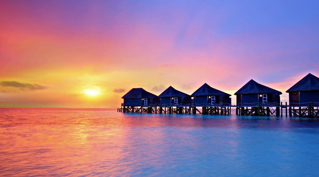 Water bungalows lined up in sea water during sunset